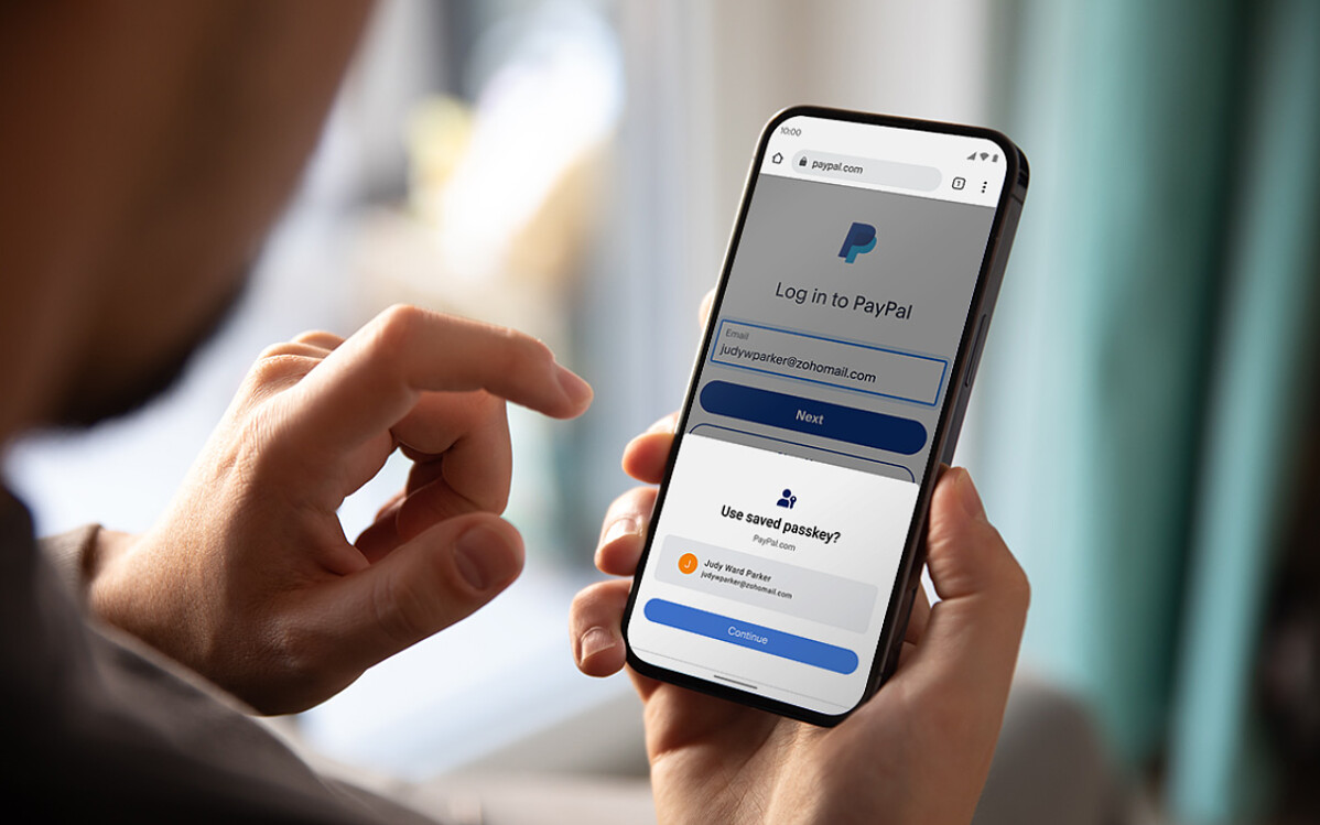 Person holding a smartphone showing the PayPal login screen.