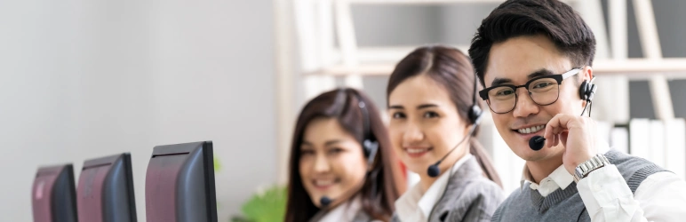 Call center support team smiling while wearing headsets at their desks.