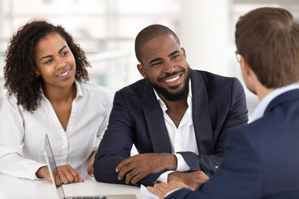 Two clients smiling during a meeting across a desk from a consultant.