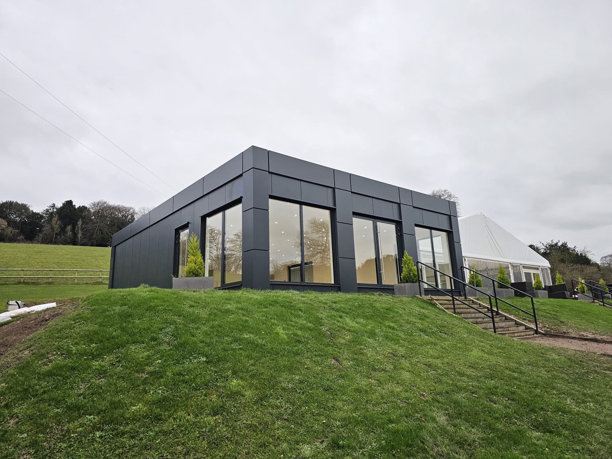 Modern dark-clad commercial building with large windows on a grassy slope.
